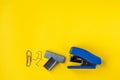 Blue stapler with metal staples and paper clip on yellow background. Top view. Copy, empty space for text. Minimalistic concept Royalty Free Stock Photo