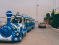 A blue steam locomotive drives through the streets of the city of Crete