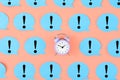 Blue stickers with exclamation marks on a pink background. In the center is a small pink alarm clock. Concept, attention