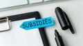 A blue sticky note with the word Subsidies written on it is on top of a clipboar. Royalty Free Stock Photo
