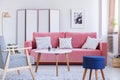 Blue stool next to wooden armchair in pastel living room interior with table and pink couch. Real photo Royalty Free Stock Photo