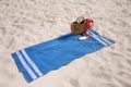 Blue striped beach towel with bag, swimsuit and accessories on sand Royalty Free Stock Photo