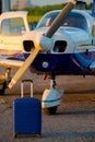 A blue suitcase and a landed small private jet. Four-seater plane with a propeller for the air taxi. Self travel concept