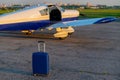 A blue suitcase and a parked small private jet. Quadruple airplane with propeller for air taxi. Self travel concept.