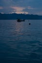 Blue sunset on calm sea with smooth waves, colorful light sky, fluffy clouds, foggy blue mountains, fishing boat on horizon. Royalty Free Stock Photo