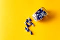 blue supplement pills spilled out of jar on yellow background Royalty Free Stock Photo