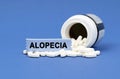 On a blue surface lies a jar of pills and a sign with the inscription - ALOPECIA