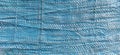 Blue synthetic burlap, close-up. Polyethylene material. Interlacing of polyethylene fibers and threads. Folds and bruises. Packing