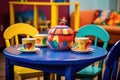 a blue teapot on a kids cafe table surrounded by colorful cups and saucers Royalty Free Stock Photo