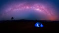 Blue tent glows under a night sky with milky way