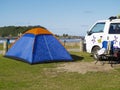 Blue tent with orange peak erected beside camper van near beach