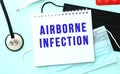 The blue text AIRBORNE INFECTION is written in a notebook that lies on a blue background next to a medical masks