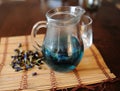 Blue Thai tea anchan in transparent glass jug on bamboo mat on wooden table. Placer of dried flowers of clitoria tea Royalty Free Stock Photo