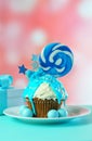 Blue novelty cupcake decorated with candy and large lollipops.