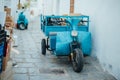 Blue three-wheeled old scooter with garbage bags and boxes near a white wall on a narrow street in the Lindos village Royalty Free Stock Photo