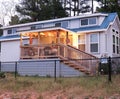 Blue tiny house in the country with warm porch lighting and a black chain fence around the yard