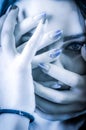 Blue toned portrait of a young woman with her face covered with hands, concept for showing the anxieties and fears of women