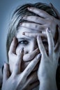 Blue toned portrait of a young woman with her face covered with hands, concept for showing the anxieties and fears of women