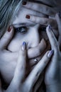 Blue toned portrait of a young woman with her face covered with hands, concept for showing the anxieties and fears of women