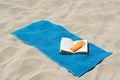 Blue towel, book and sunscreen on sandy beach