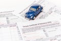Blue toy car on insurance documents on white