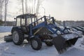 Blue tractor with a blade for snow removal in winter and a spinning brush for street cleaning