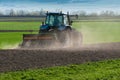 Blue tractor equipped with harrow working on the field