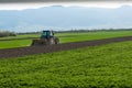 Blue tractor equipped with harrow working on the field