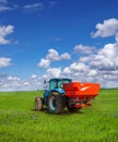 Blue tractor in field work with modern red two-disc fertiliser spreader sprayer, Features of spring feeding of winter cereals