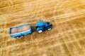 Blue Tractor Towing a Trailer Through Golden Wheat Field During Harvest Season Royalty Free Stock Photo