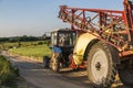 A blue tractor with a trailer for agricultural works rides along a road in a wheat field.