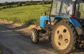 A blue tractor with a trailer for agricultural works rides along a road in a wheat field.