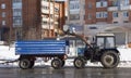 A blue tractor with a trailer clears the snow, clearing the city .Cleaning of the territory by public utilities in winter Royalty Free Stock Photo