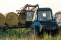 The blue tractor uses a hydraulic manipulator to stack round bales of hay in pyramids for storage and drying. Machinery works in