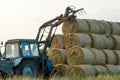 The blue tractor uses a hydraulic manipulator to stack round bales of hay in pyramids for storage and drying. Machinery works in