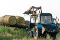 The blue tractor uses a hydraulic manipulator to stack round bales of hay in pyramids for storage and drying. Machinery works in