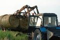 The blue tractor uses a hydraulic manipulator to stack round bales of hay in pyramids for storage and drying. Machinery works in