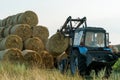 The blue tractor uses a hydraulic manipulator to stack round bales of hay in pyramids for storage and drying. Machinery works in