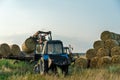 The blue tractor uses a hydraulic manipulator to stack round bales of hay in pyramids for storage and drying. Machinery works in