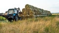 The blue tractor uses a hydraulic manipulator to stack round bales of hay in pyramids for storage and drying. Machinery works in