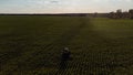 A blue tractor is working in a green field at sunset