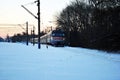 Blue train in snowy park, railroad along trees line, winter