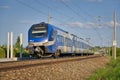 blue train on tracks under overhead power lines at a station