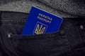 A blue Ukraine international biometric passport in a pocket of black jeans.