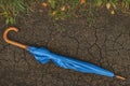 Blue umbrella on dry ground with crackling and yellow leaves. Fall autumn scene. Conceptual image of dry land and Royalty Free Stock Photo