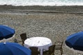 Blue umbrellas, reserved tables with white tablecloths on the pebble beach of the Promenade des Anglais in Nice, France, await gue Royalty Free Stock Photo