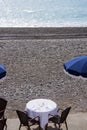 Blue umbrellas, reserved tables with white tablecloths on the pebble beach of the Promenade des Anglais in Nice, France, await gue Royalty Free Stock Photo