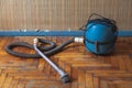 Blue vacuum cleaner stands on shabby parquet floor