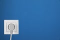 Blue wall with power socket and inserted plug. Electrical supply Royalty Free Stock Photo