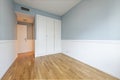 Blue walled room with a built-in wardrobe with three white lacquered doors with golden handles and oak wood floors